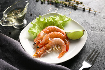Plate with tasty boiled shrimps, lettuce and lime on black background