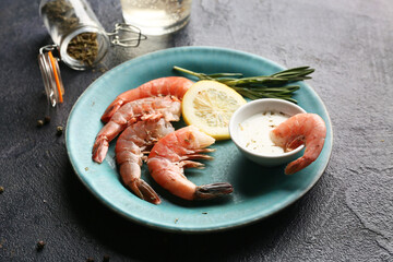 Plate with tasty boiled shrimps and bowl of sauce on dark background