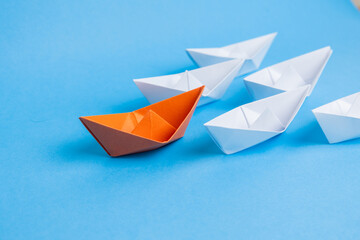 orange paper boat leading white boats on blue backgroun, leadership and business concept.