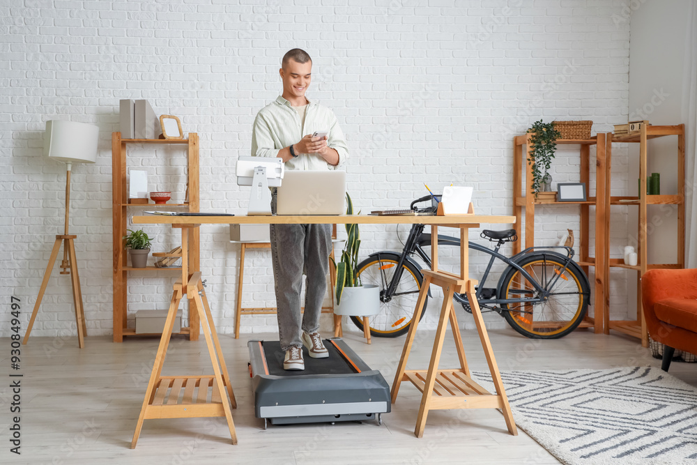 Sticker Young man working with mobile phone on treadmill at table in office