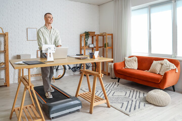 Young man working with laptop on treadmill at table in office