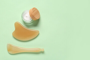 Facial massage tools and jar of cosmetic product on green background