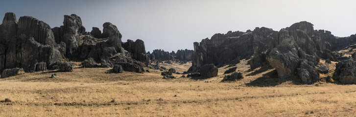 A wide rocky plain marked with rugged rock formations and casting shadows stretches under a clear...