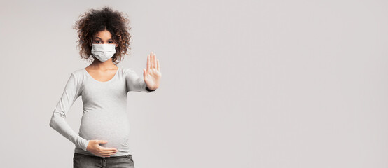 Infectious diseases and flu. Pregnant lady in medical mask gesturing stop sign, gray background