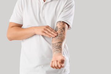 Young man with his tattooed hand in protective film on light background, closeup