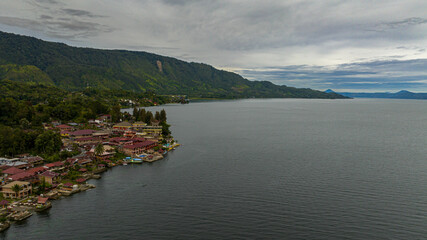Fototapeta premium Aerial drone of Tourist spot Tuk Tuk on Lake Toba and the coast of Samosir Island. Sumatra, Indonesia. Tropical landscape.
