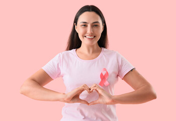 Young woman with pink ribbon making heart gesture on color background. Breast cancer awareness concept