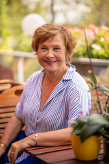 Smiling woman seated at a wooden table in a garden with vibrant