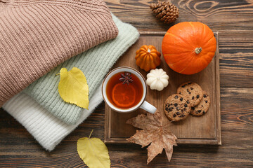 Composition with cup of tea, cookies, sweaters and autumn decor on wooden background