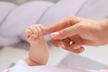 Little baby holding woman's finger in bedroom, closeup