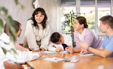 Fototapeta premium Young teacher discussing her notes with group of grown-up students excitedly around the table
