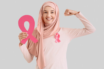 Young Muslim woman with pink ribbons showing muscles on light background. Breast cancer awareness...