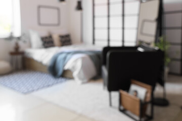 Blurred view of light bedroom with armchair, mirror and folding screen