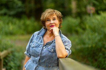 Woman in denim jacket poses thoughtfully by wooden railing in a