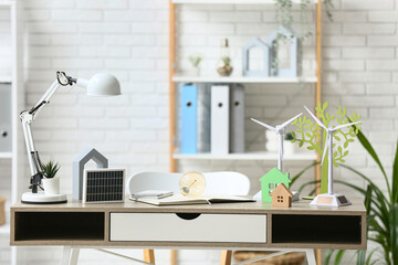 Wind turbine models with light bulb, house figures and solar panel on table in office. Green Energy concept