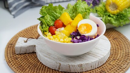 A bowl of salad with corn, egg, mango, tomato, lettuce, red cabbage