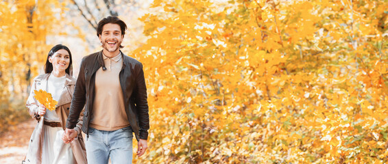 Obraz premium Excited guy showing his pretty girlfriend beautiful autumn forest, pulling her hand, copy space