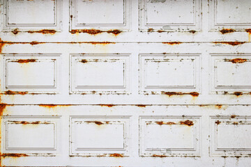 Badly damaged by harsh whether elements metal garage door with rusty spots over white paint, backdrop or background