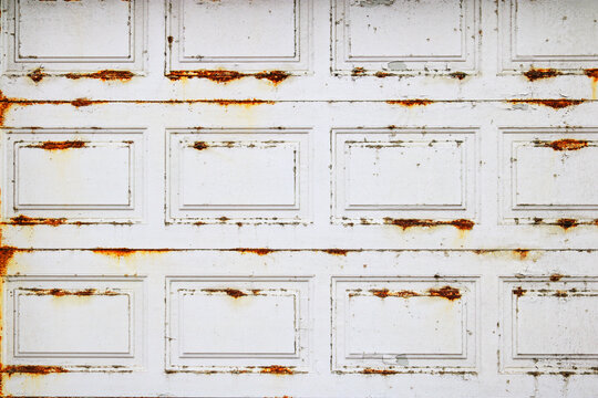 Badly damaged by harsh whether elements metal garage door with rusty spots over white paint, backdrop or background