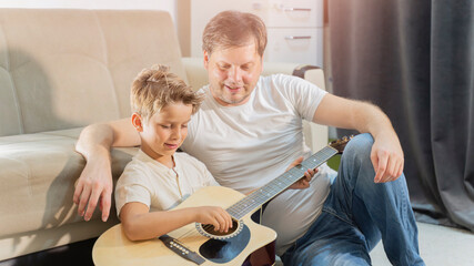 The boy is a musician, the child is engaged in music, playing the guitar with his teacher and his dad at home