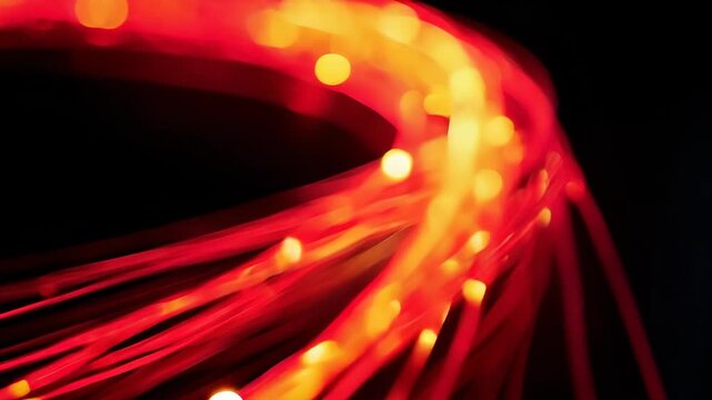 Illuminated fiber optic strands swirl in darkness. Vibrant red and yellow light trails create a sense of speed and connectivity. Motion blur enhances the dynamic visual effect.	