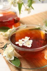 Hot jasmine tea in cup and flowers on white table, closeup