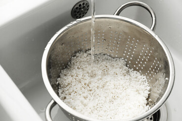 Pouring water into colander with rice in sink, closeup