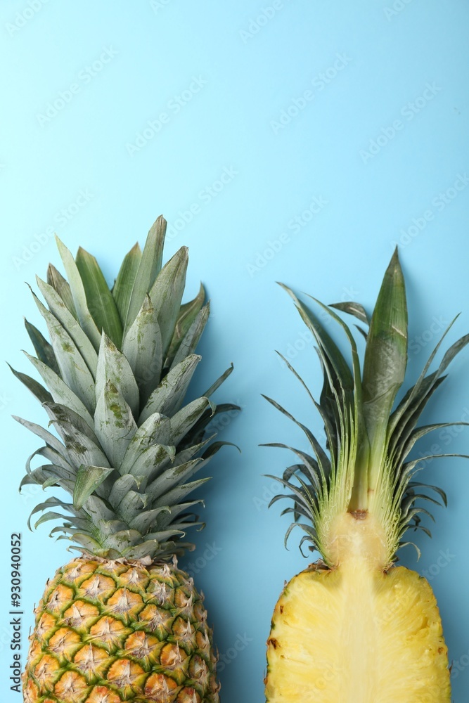 Wall mural Whole and cut ripe pineapples on light blue background, flat lay. Space for text