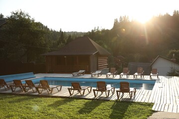 Outdoor swimming pool, sunbeds and houses near forest on sunny day