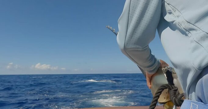 Rear view of man on fishing boat reeling in big fish