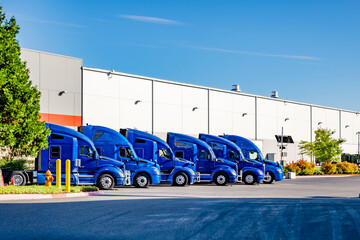 Long hauler blue industrial carrier big rig semi trucks standing in row on the warehouse parking...