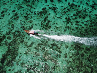 Aerial view of the turquoise water of Phi Phi islands in Krabi, with coral reefs and a long tail boat leaving a wake as it passes, Thailand