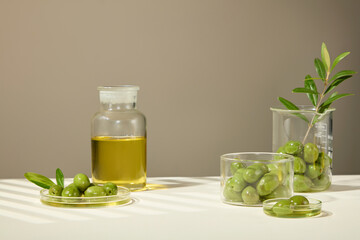 Olives and extract are placed in various containers such as beakers, petri dishes, and glass jars, with a designated space in the middle for the product. Cosmetics advertisement.