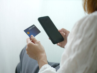 Woman sitting shopping online, using a smartphone, placing a cre