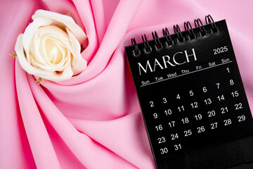 March 2025 desk calendar black color and rose on pink background.