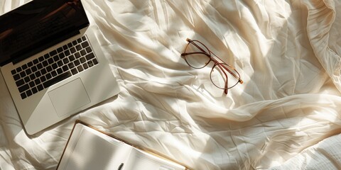 Blank paper card sheets with copy space glasses laptop on rumpled bed linen with aesthetic warm sunlight shadows Flat lay top view