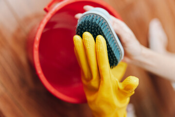 Person in yellow rubber gloves cleaning floor with brush and bucket of water