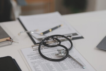 Doctor's working on laptop computer, writing prescription clipboard with record information paper folders on desk in hospital or clinic, Healthcare and medical concept. Focus on stethoscope