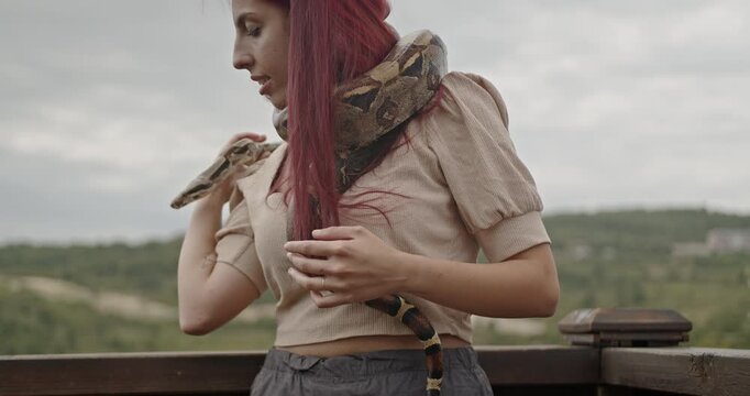 A young woman with long red hair holds her pet snake around her neck.