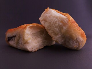 Two golden-brown baked rolls, one cut open to show its soft interior, are presented simply on a dark, plain background
