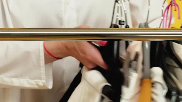 Shopping sale. Capsule wardrobe. Unrecognizable female assistant hands taking away clothes on hangers isolated on yellow background.