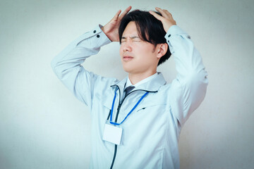 頭を抱える作業服着た男性
A man wearing work clothes holding his head