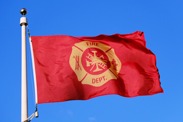 A red Fire Department Flag waving against a blue sky background