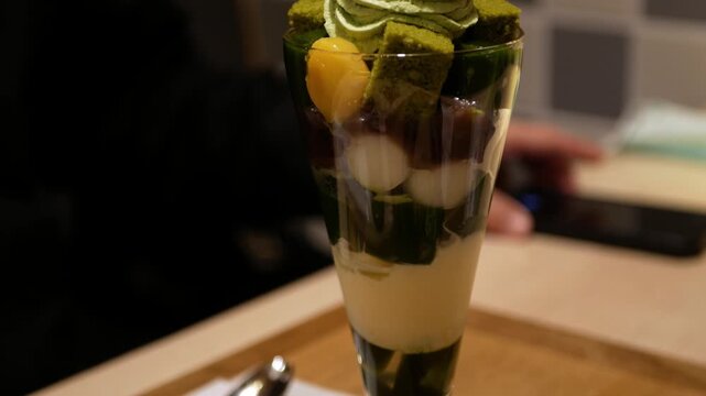 tilt down close up view to beautiful parfait sweet dessert in japanese style full with ice cream mochi green tea yelly and topped with green tea cream in japanese minimal cafe