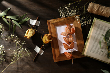 Dried flowers and plants, photo frame, book and twine on wooden background, top view