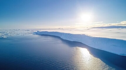 Aerial view of a large iceberg in a frozen ocean landscape, with a bright blue sky and sunshine.