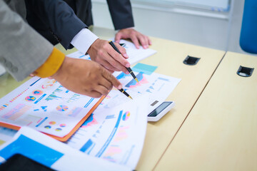 Two businessmen are seated at a desk in an office, engaged in a meeting focused on analysis, finance, and marketing strategies, with documents and graphs spread across the table.