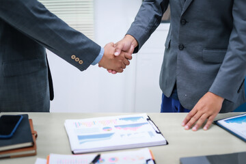 Two businessmen are seated at a desk in an office, engaged in a meeting focused on analysis, finance, and marketing strategies, with documents and graphs spread across the table.