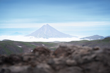 in the distance, the Vilyuchinsky volcano stands above the clouds in the valley, with a rocky rock in the foreground