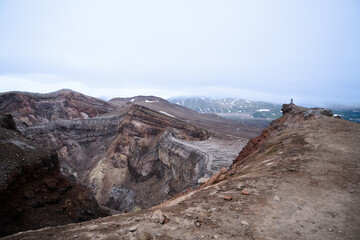 on the edge of the cliff - crater of the Gorely volcano, a girl stands and looks into the abyss, in the distance there is still a chain of volcanoes in the clouds and fog